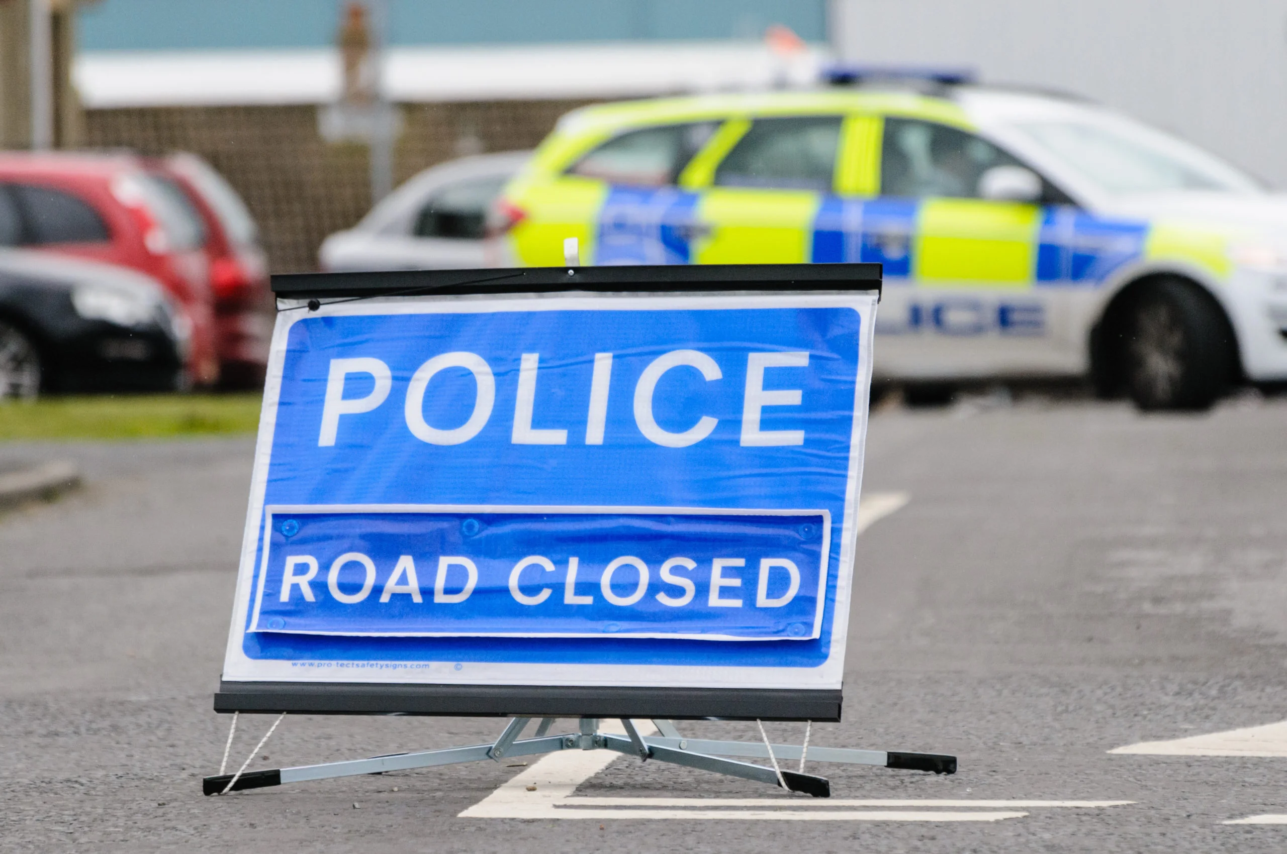 Police road closed sign with police car blocking the road