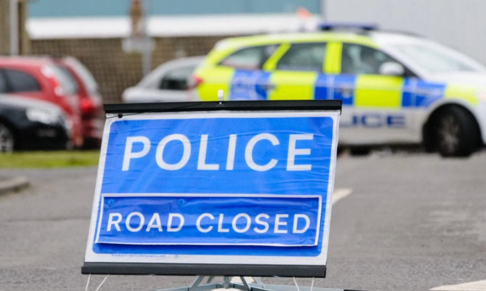 Police road closed sign with police car blocking the road