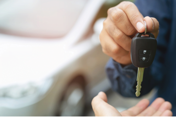 Someone receiving keys, handed over by another person - with a car in the background